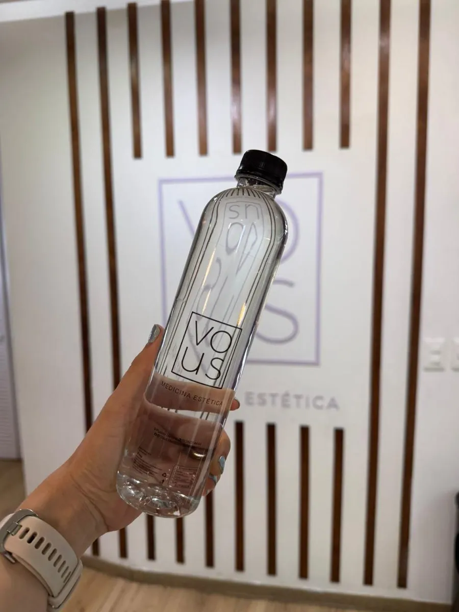 Mano sosteniendo una botella de 500 ml con etiqueta transparente de una clínica de medicina estética